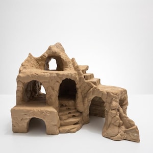 May include: A tan, textured, multi-level rock-like structure featuring several arched openings, carved staircases, and hollow chambers. This decorative piece mimics a natural cave formation with rugged, uneven surfaces and multiple levels for exploration.