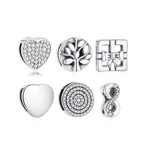May include: A collection of silver charms with various designs. Includes a heart covered in small clear stones, a charm with a tree design, a gift box with a bow, a plain heart, a charm with a spiral of clear stones, and an infinity symbol.