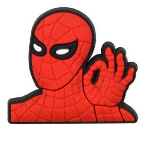 May include: A red and black rubberized shoe charm featuring a character with a webbed pattern mask and white eyes, depicted making an okay hand gesture. The design is flat with raised details and a thick black border outlining the entire shape.