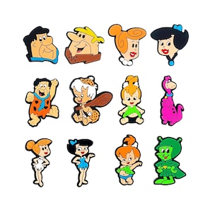 May include: A set of twelve colorful shoe charms featuring various cartoon characters from The Flintstones, including Fred, Wilma, Barney, Betty, Pebbles, Bamm-Bamm, Dino, and the Great Gazoo, rendered in a flat, molded PVC style with distinct outlines.