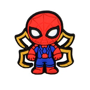 May include: A rubberized shoe charm featuring a stylized character with a red mask, white eyes, and a blue and red suit. The character has four yellow spider-like legs extending from the sides, all outlined in black against a plain white background.