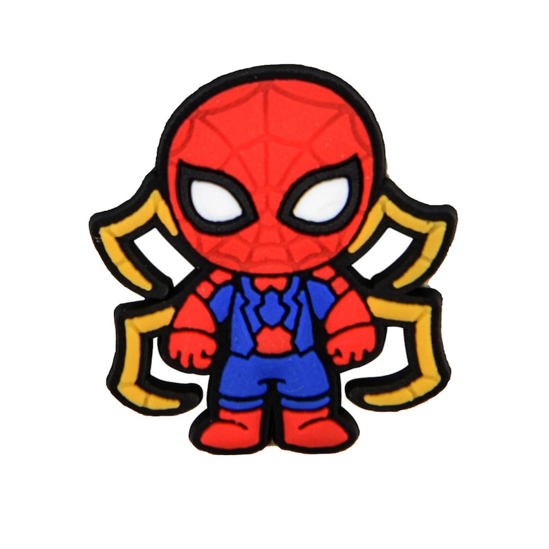May include: A rubberized shoe charm featuring a stylized character with a red mask, white eyes, and a blue and red suit. The character has four yellow spider-like legs extending from the sides, all outlined in black against a plain white background.