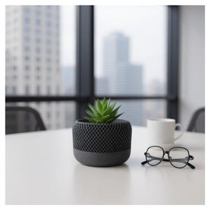 Pode incluir: Um pequeno vaso cinza escuro com um design de malha geométrica, contendo uma planta suculenta verde. Uma caneca branca e óculos com armação preta estão sobre uma mesa branca. Ao fundo, uma paisagem urbana.