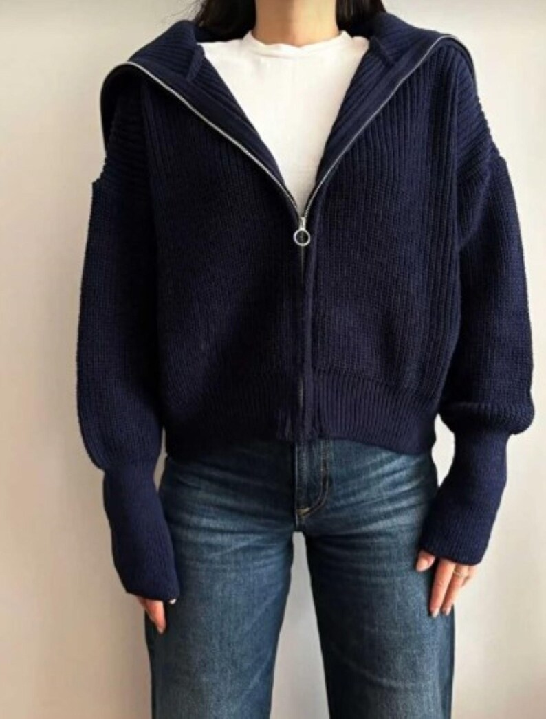 May include: A navy blue zip-up hooded sweater with a silver zipper. The sweater has a ribbed knit texture and long sleeves. The person is wearing blue jeans and a white t-shirt underneath the sweater.