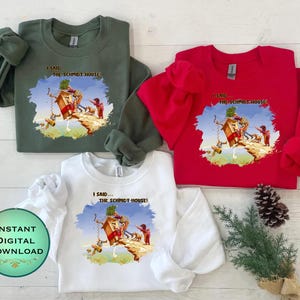 Può includere: Tre felpe, verde, rossa e bianca, ciascuna con una grafica colorata e la scritta "I SAID THE SCHMIDT HOUSE!". La grafica raffigura una scena stravagante con figure e una casa. Le felpe sono disposte su una superficie di legno chiaro.