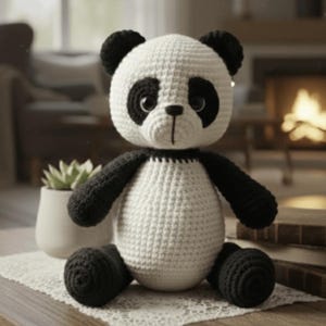 Könnte beinhalten: Ein handgehäkelter Panda-Bär in Schwarz und Weiß. Der Panda hat schwarze Ohren, Augen, Arme und Füße, mit einem weißen Körper und Kopf. Der Panda sitzt auf einer Holzoberfläche.