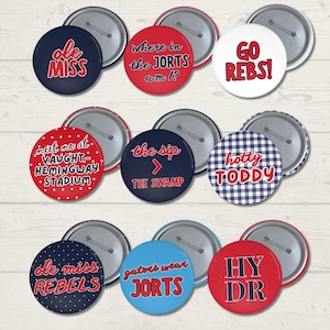 Puede incluir: Una colección de nueve chapas redondas con diversos diseños en rojo, blanco y azul. Los botones muestran textos que incluyen Ole Miss, Where in the JORTS am I?, GO REBS!, meet me at VAUGHT-HEMINGWAY STADIUM, the sip > THE SWAMP, hotty TODDY, ole miss REBELS, gators wear JORTS y HY DR.