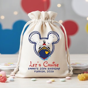 May include: A cream-colored drawstring bag featuring a Mickey Mouse-shaped outline with a cruise ship design. The text "Let's Cruise" and birthday details are printed in red and blue. The bag is filled with treats.