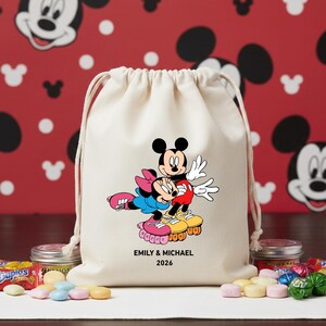 May include: A cream-colored drawstring bag featuring Mickey and Minnie Mouse on roller skates. The cartoon characters are in a loving embrace. The bag has the text "EMILY & MICHAEL 2026" printed on it. The background is red with white Mickey Mouse silhouettes.