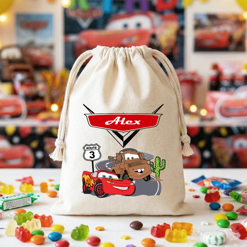 Puede incluir: Una bolsa de algod&oacute;n beige con cord&oacute;n que presenta un gr&aacute;fico rojo y blanco con el nombre Alex dentro de un logotipo de coche, con ilustraciones de un coche de carreras rojo, una gr&uacute;a marr&oacute;n, una se&ntilde;al de Ruta 3 y un cactus verde.
