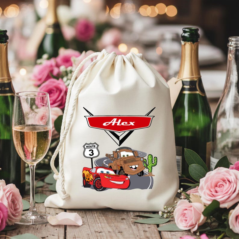 Puede incluir: Una bolsa de color crema con cord&oacute;n que presenta un estampado gr&aacute;fico de un coche de carreras rojo y una gr&uacute;a marr&oacute;n en una carretera con un cactus. Sobre los veh&iacute;culos hay un emblema rojo con el nombre Alex y una se&ntilde;al de Ruta 3.