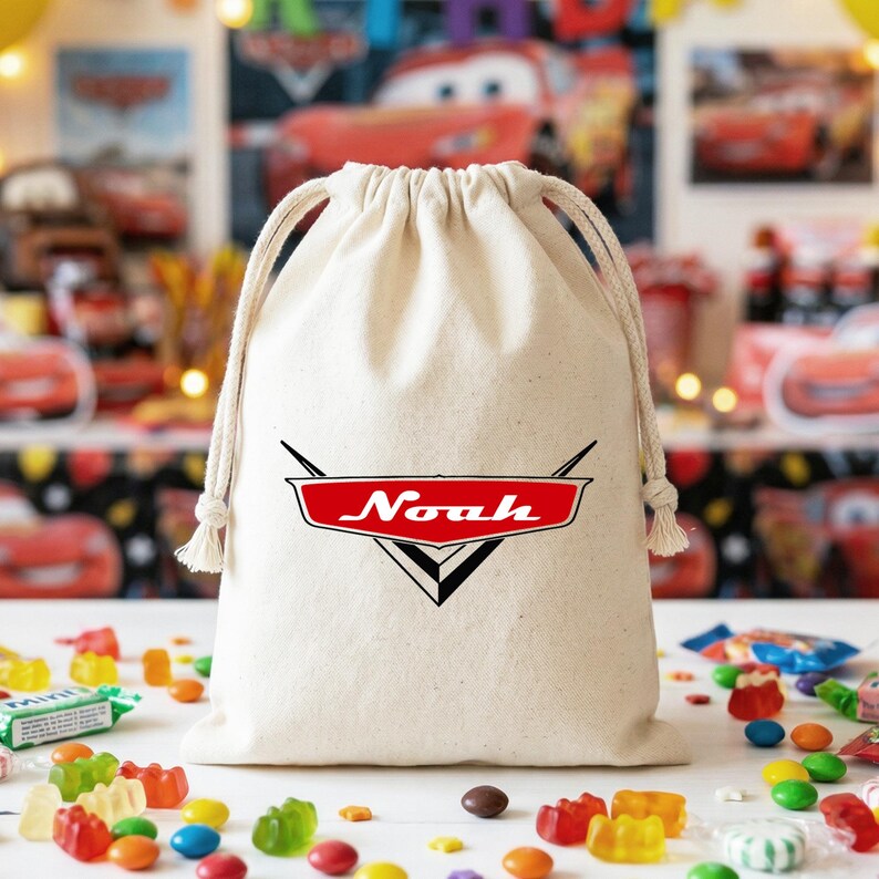 May include: A natural-colored cotton drawstring bag featuring a red and black graphic logo inspired by the Cars movie franchise, with the name Noah printed in white script across the center of the red emblem, finished with thick braided cords.