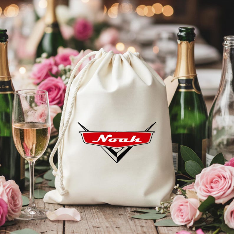 May include: A cream-colored fabric drawstring bag featuring a red and black graphic emblem with the name Noah printed in white script. The bag is made of a smooth, opaque material and includes thick white cord strings for closure at the top.