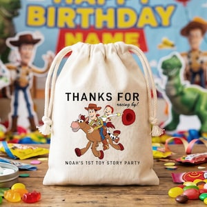 May include: A beige drawstring bag with a cartoon image of Woody and a child riding a horse. The bag has the text "THANKS FOR racing by!" and "NOAH'S 1ST TOY STORY PARTY". The background includes Toy Story character cutouts and a birthday banner.