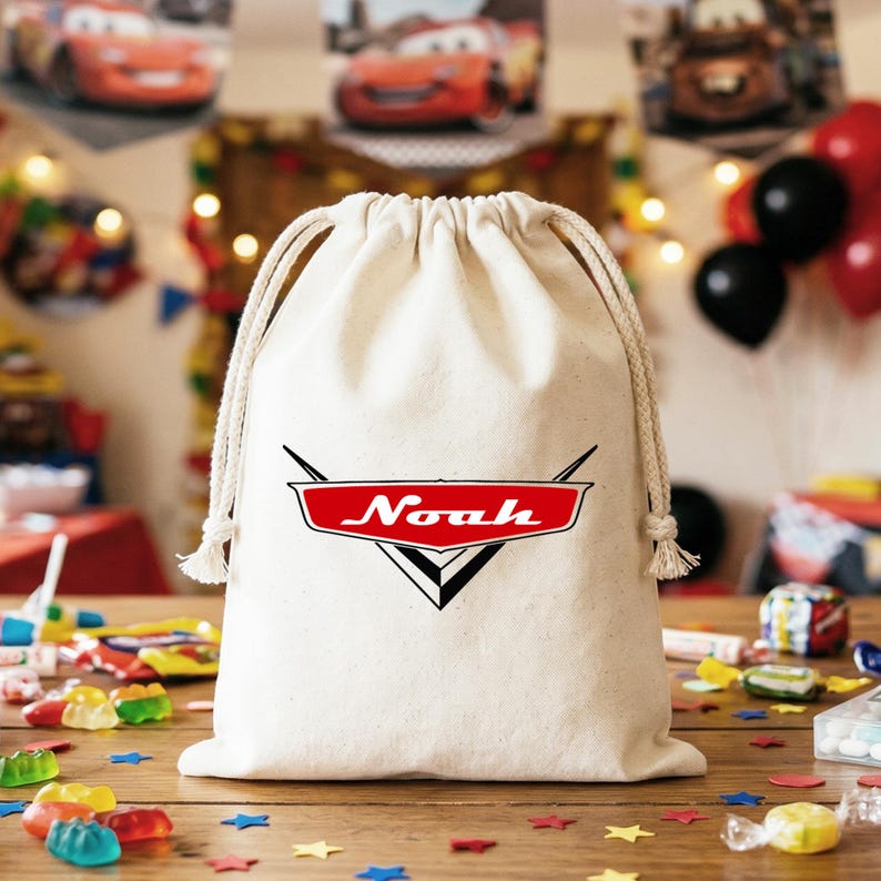 May include: A natural-colored canvas drawstring bag featuring a red and black graphic emblem on the front. The emblem is shaped like a stylized car hood ornament with the name Noah printed in white script across the center of the red section.