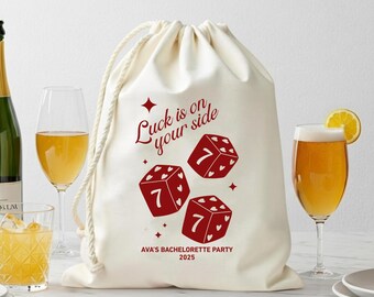 Könnte beinhalten: Ein cremefarbener Kordelzugbeutel mit roten Würfelgrafiken und dem Text "Luck is on your side". Der Beutel enthält auch den Text "AVA'S BACHELORETTE PARTY 2025". Das Bild zeigt Champagner, Cocktails und Bier.