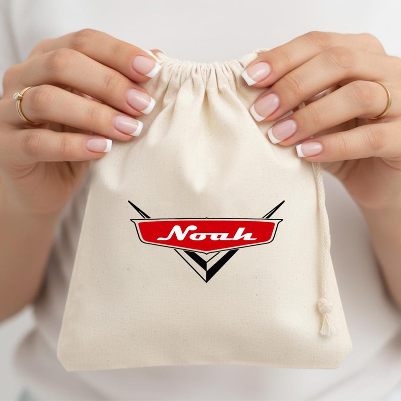 May include: A cream-colored fabric drawstring pouch featuring a red and black graphic emblem on the front. The emblem is shaped like a stylized car logo with the name Noah printed in white script lettering across the center of the red section.