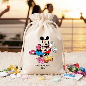 May include: A cream-colored drawstring bag featuring a colorful graphic of Mickey and Minnie Mouse on roller skates. The text "EMILY & MICHAEL 2026" is printed below the characters. Candy is scattered around the bag.
