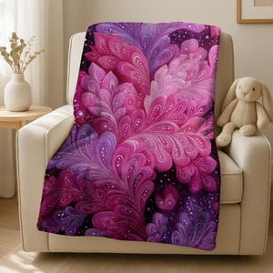 May include: A plush throw blanket draped over a chair, featuring a vibrant floral design in shades of pink, purple, and magenta. The pattern has a detailed, feathery appearance with white accents, set against a dark background. A stuffed bunny sits on the chair.