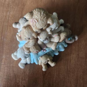 Puede incluir: Una figura con una pila de osos de peluche en varios tonos de beige y blanco. Los osos est&aacute;n colocados sobre una base azul claro con volantes. Los osos tienen ojos peque&ntilde;os y oscuros y est&aacute;n en una pose juguetona.