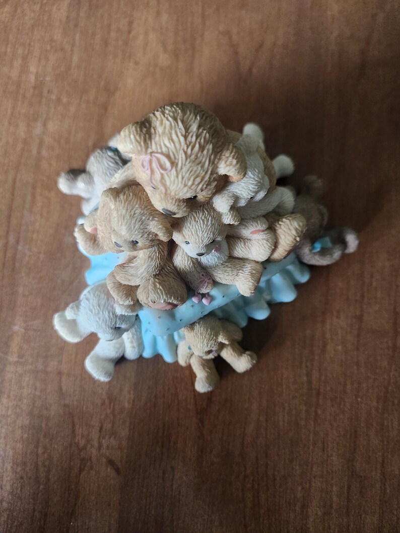 Puede incluir: Una figura con una pila de osos de peluche en varios tonos de beige y blanco. Los osos est&aacute;n colocados sobre una base azul claro con volantes. Los osos tienen ojos peque&ntilde;os y oscuros y est&aacute;n en una pose juguetona.