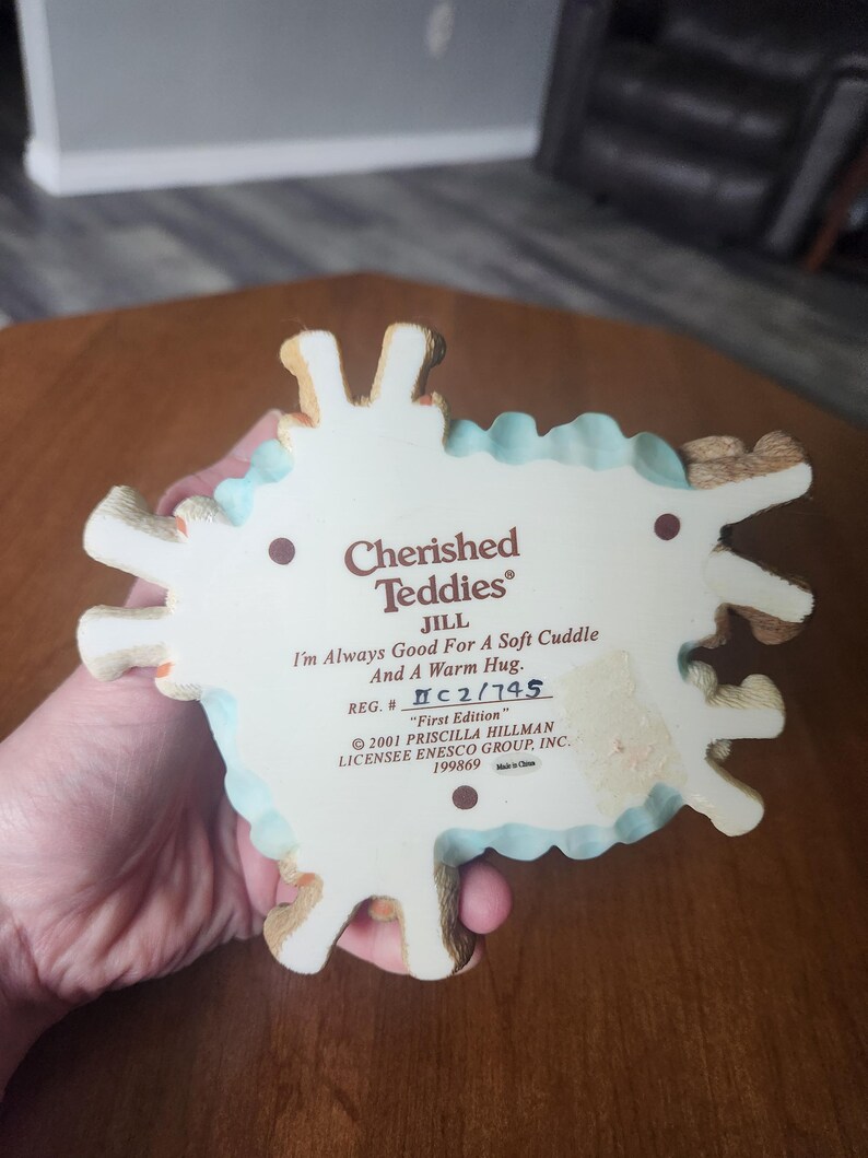 Puede incluir: Una figura de Cherished Teddies, con Jill, con el texto "I'm Always Good For A Soft Cuddle And A Warm Hug." La base es blanca con un borde festoneado azul claro y detalles de osito de peluche marr&oacute;n. Tambi&eacute;n est&aacute; impresa "First Edition".