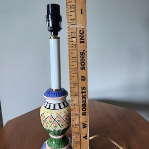 May include: A colorful ceramic table lamp with a white stem and a patterned base. The base features blue, green, yellow, and pink designs. The lamp is approximately 16 inches tall.