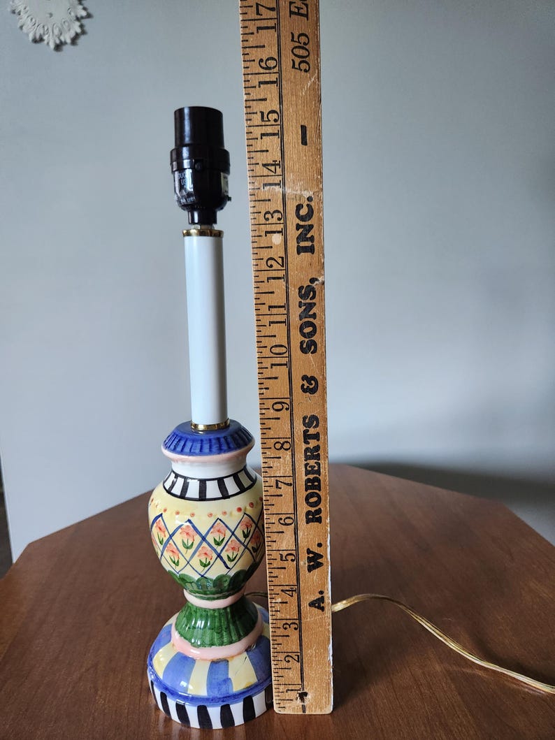 May include: A colorful ceramic table lamp with a white stem and a patterned base. The base features blue, green, yellow, and pink designs. The lamp is approximately 16 inches tall.