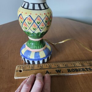 May include: A colorful ceramic table lamp with a painted floral design. The lamp features a blue, yellow, and green base with a matching top. The lamp is approximately 9 inches tall.