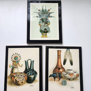 May include: Three framed prints featuring Native American art. The top print shows a kachina figure in a headdress. The bottom left print depicts a kachina figure with pottery. The bottom right print displays a vase, pottery, and feathers.