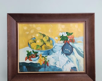 May include: A framed still life painting featuring a bowl of yellow-green fruit, a blue vase with flowers, and small bowls of red peppers. The painting has a yellow background and a white tablecloth.
