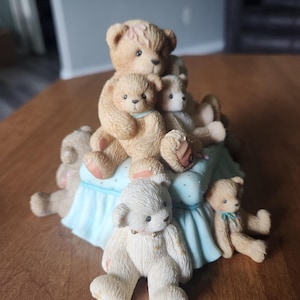 Puede incluir: Figura decorativa con un grupo de osos de peluche. Los osos est&aacute;n en varias poses, algunos sentados y otros tumbados. La figura tiene una base azul claro con lunares blancos. Los osos son de color marr&oacute;n y blanco.
