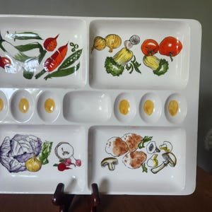 May include: White divided serving tray with hand-painted vegetable illustrations. Features compartments for various foods, including eggs, tomatoes, and mushrooms. A vintage-style serving dish for appetizers or snacks.