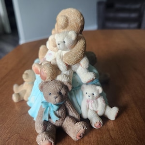 Puede incluir: Una figura de osos de peluche. La figura central es un oso marr&oacute;n m&aacute;s grande que sostiene varios osos m&aacute;s peque&ntilde;os. Un oso marr&oacute;n tiene un lazo azul y otro es blanco con un lazo rosa. Los osos est&aacute;n sobre una base azul claro.