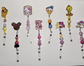 May include: A collection of badge reels featuring cartoon characters like Winnie the Pooh, Hello Kitty, and Donald Duck. Each reel has a unique design with colorful beads and a clear plastic clip for attaching to clothing or accessories.