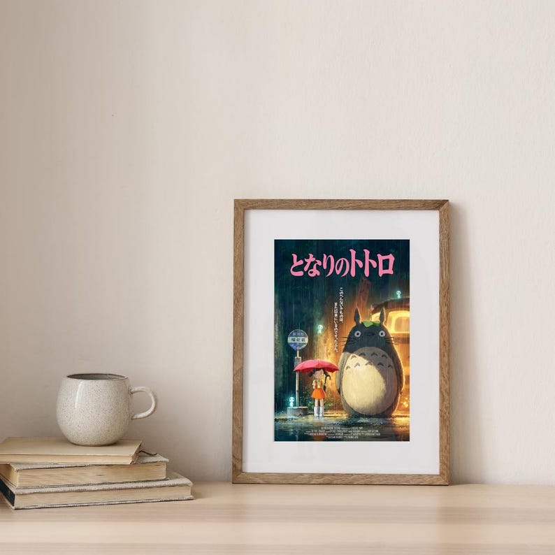 K&ouml;nnte beinhalten: Gerahmtes Poster mit einer Szene aus dem Animationsfilm "Mein Nachbar Totoro". Das Kunstwerk zeigt einen gro&szlig;en, pelzigen Totoro-Charakter, der im Regen steht, und ein junges M&auml;dchen mit einem Regenschirm. Der Titel ist in rosa japanischen Schriftzeichen.