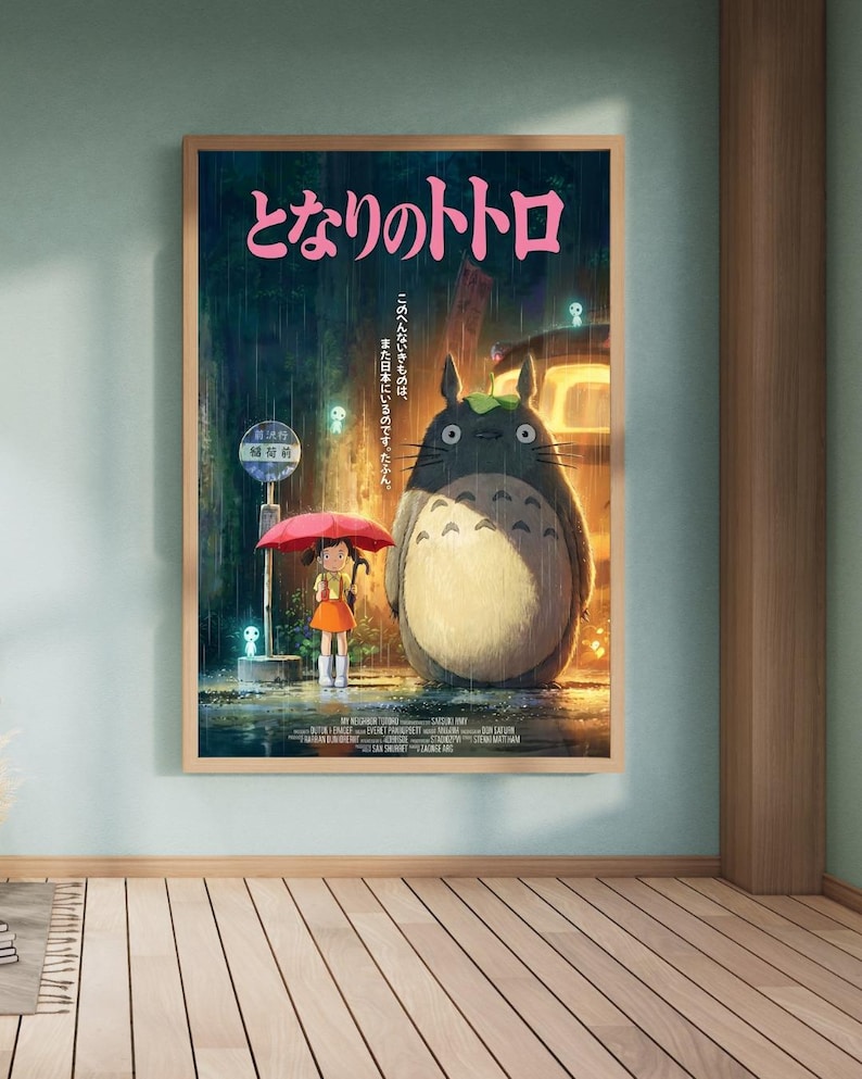 K&ouml;nnte beinhalten: Ein gerahmtes Poster des Zeichentrickfilms "Mein Nachbar Totoro." Das Kunstwerk zeigt ein junges M&auml;dchen mit rotem Regenschirm an einer Bushaltestelle mit Totoro im Regen. Japanischer Text ist oben sichtbar.