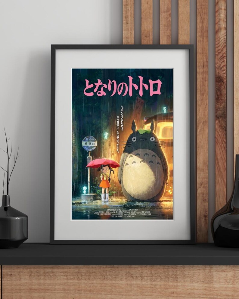K&ouml;nnte beinhalten: Gerahmtes Poster mit dem Zeichentrickfilm "Mein Nachbar Totoro". Das Kunstwerk zeigt ein junges M&auml;dchen mit einem roten Regenschirm, das neben einer gro&szlig;en, pelzigen Kreatur in einer regnerischen Szene steht. Japanischer Text ist oben sichtbar.