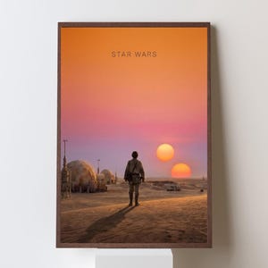 Op de afbeelding: Een ingelijste Star Wars kunstprint. De afbeelding toont een figuur die op een woestijnplaneet loopt onder een dubbele zonsondergang. De print heeft een bruine lijst en de tekst "STAR WARS" staat bovenaan.