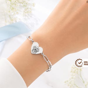 May include: A silver-toned chain bracelet featuring a central heart-shaped charm engraved with a detailed line drawing of a dog's face. The bracelet consists of elongated oval links and secures with a clasp, showcasing a custom pet portrait design.