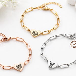 May include: Three link chain bracelets with heart-shaped charms. One gold bracelet features a dog engraving, one rose gold bracelet features a cat engraving, and one silver bracelet features a rabbit engraving. Each includes a lobster clasp closure.