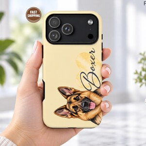 Op de afbeelding: Een lichtgeel smartphonehoesje met een gedetailleerde illustratie van het gezicht van een Duitse herder aan de onderkant en het woord Boxer in zwarte cursieve letters naast een vage gele hartvorm aan de rechterbovenkant.