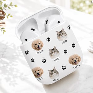 Könnte beinhalten: Eine weiße Schutzhülle für kabellose Ohrhörer mit einem sich wiederholenden Muster aus Katzen- und Hundegesichtern, wobei unter jedem Tier die Namen Milo und Coco stehen, durchsetzt mit kleinen schwarzen Pfotenabdrücken auf der Oberfläche.