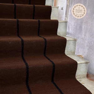 May include: Brown stair runner with black vertical stripes. The runner is installed on a set of concrete stairs. The Rugs Empires logo is visible in the upper right corner. The runner adds a decorative element to the staircase.