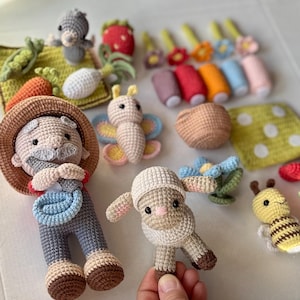 May include: A collection of handmade crochet toys, including a farmer, a sheep, a bee, a butterfly, and various vegetables and flowers. The toys are in various colors, including beige, brown, yellow, blue, and red. The farmer is wearing a straw hat and overalls.