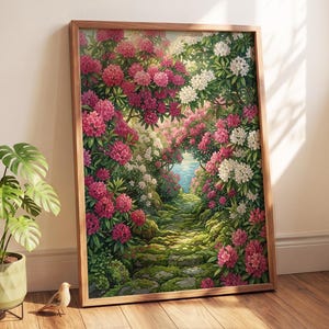 May include: A framed vertical wall art print depicting a stone path winding through a lush garden filled with vibrant pink and white rhododendron flowers, with a glimpse of blue water in the distance, set in a simple light brown wooden frame.
