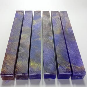 May include: Seven rectangular blocks with a marbled appearance. The blocks are primarily purple with streaks of gold and brown. The blocks are arranged side by side on a white surface. The blocks appear to be made of a solid material.