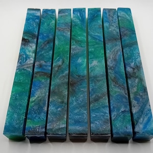 Può includere: Otto blocchi rettangolari con un motivo marmorizzato nelle tonalità del blu, verde e grigio. I blocchi sono disposti uno accanto all'altro, mostrando i vari modelli e colori all'interno del materiale. I blocchi hanno una superficie lucida e liscia.