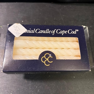 Può includere: Una scatola rettangolare blu navy contenente candele affusolate ritorte color bianco sporco. La scatola presenta la scritta Colonial Candle of Cape Cod e un logo dorato con tre cerchi intrecciati. Un piccolo cartellino del prezzo bianco.