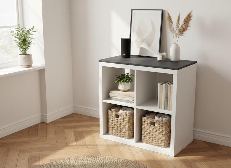 May include: A white and black cube storage unit with woven baskets, books, and decorative items. A black speaker sits on top. A framed abstract art print and a vase with dried plants are also displayed.